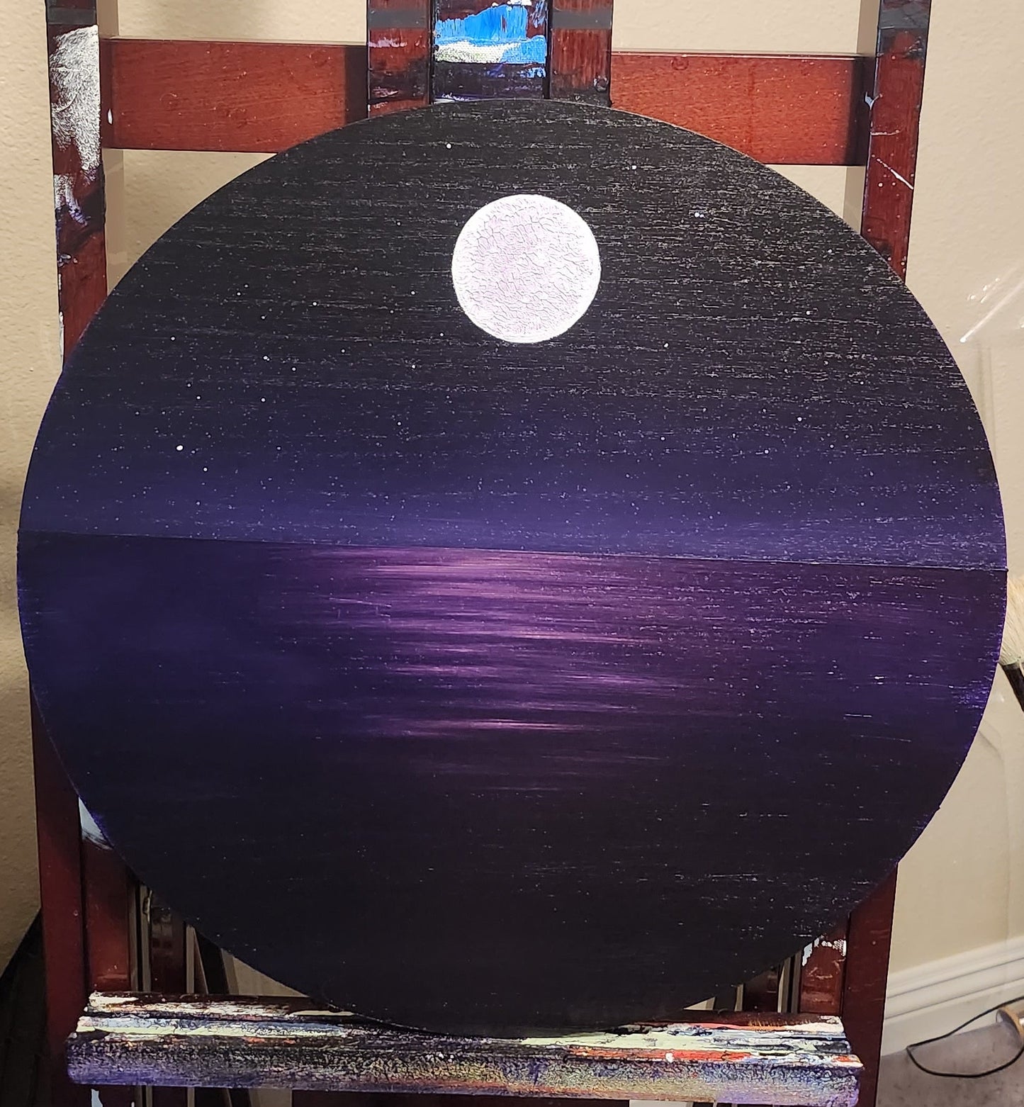 Gold Reflections Original Painting: A painting on a circle wood panel on an easel of a full moon and night sky and a pink highlighted ocean