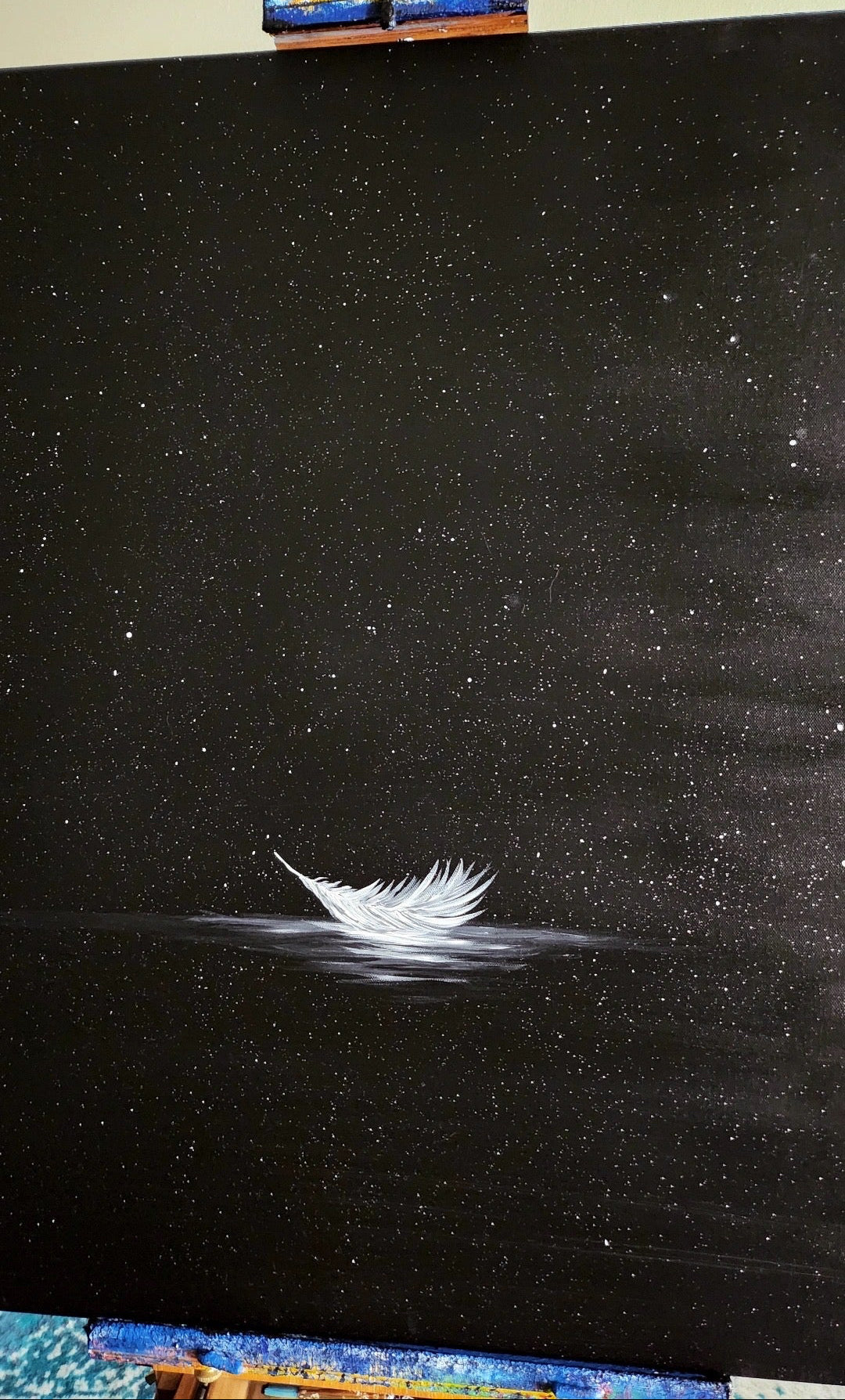 A painting of a white feather on a black surface with a starry night sky background