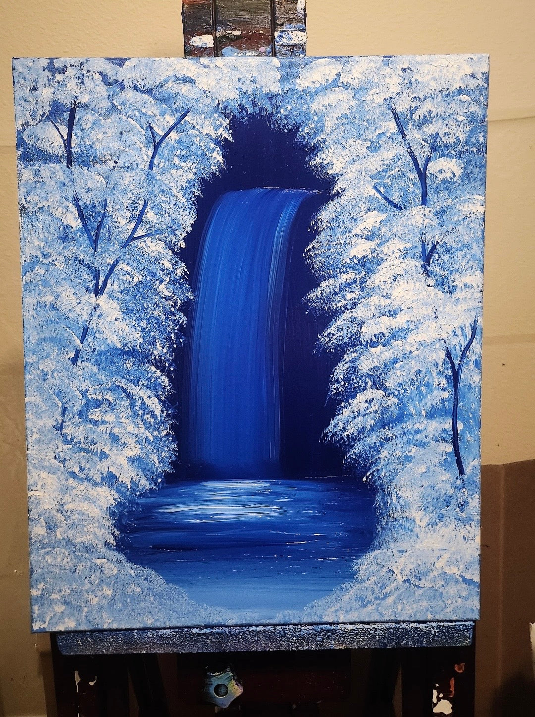 Painting of a waterfall surrounded by snow-covered trees on an easel.