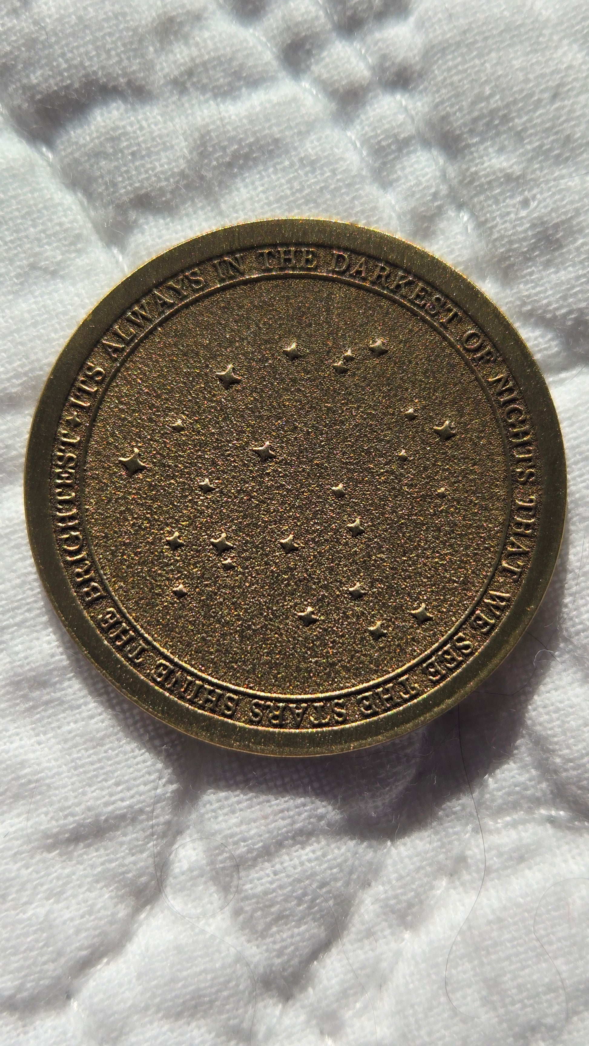 Bronze coin with engraved text and star patterns on a white fabric background