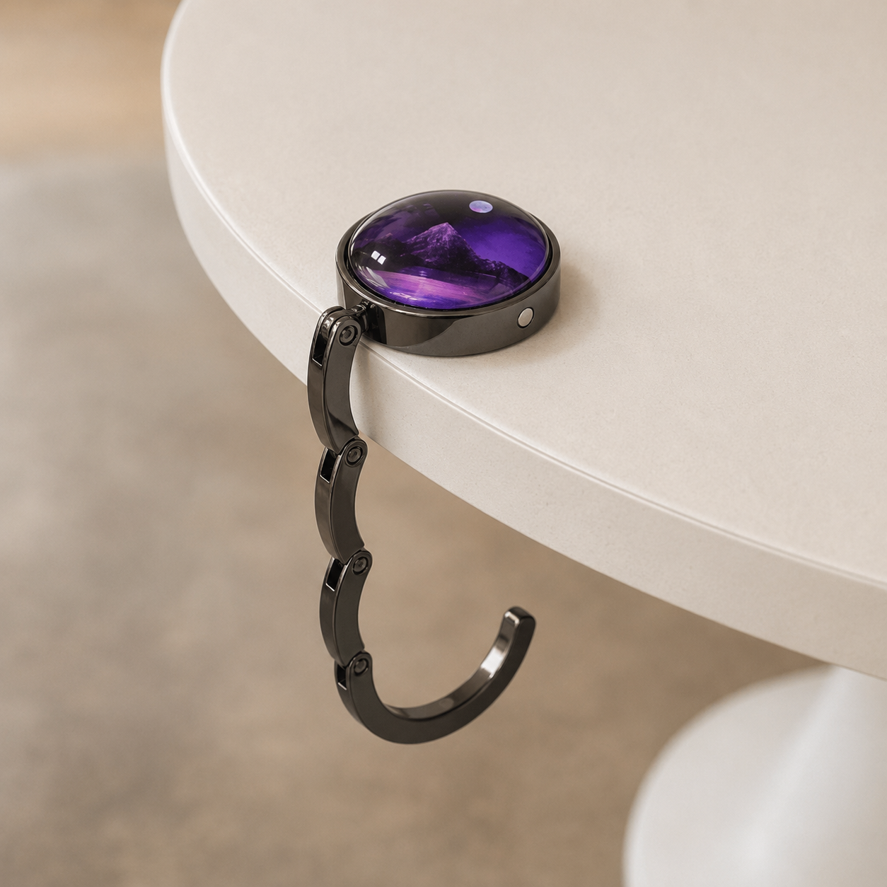 A black circular bag hook on the edge of a white round table, with its hook-shaped bracket hanging down over the table edge.