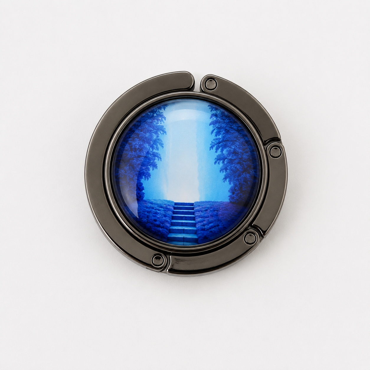 A circular black metal bag hook folded up with a glossy blue painting depicting a pathway leading up steps between dark trees, shown on a white background.
