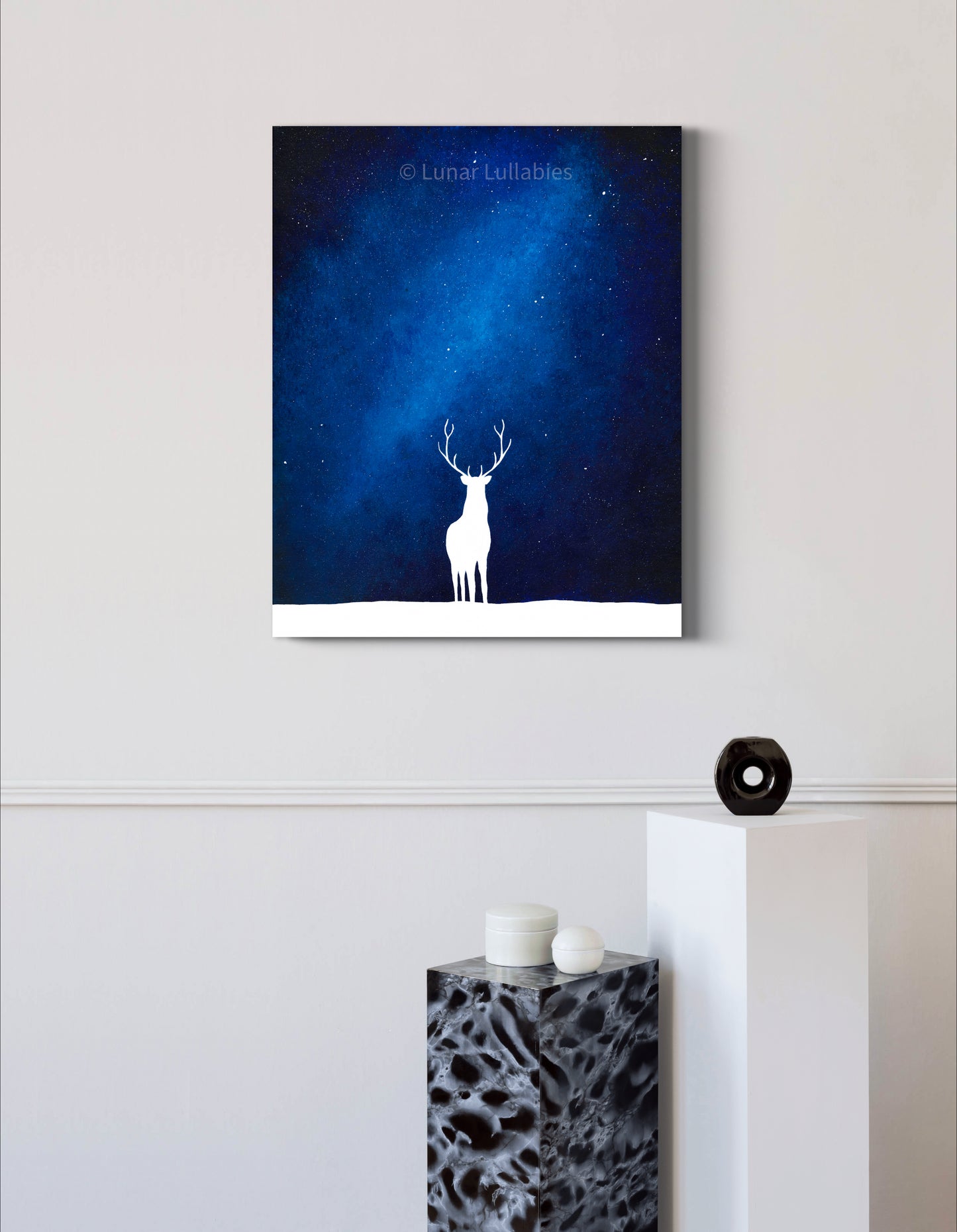 Mockup: Artwork of a white deer silhouette against a blue night sky on a white wall.