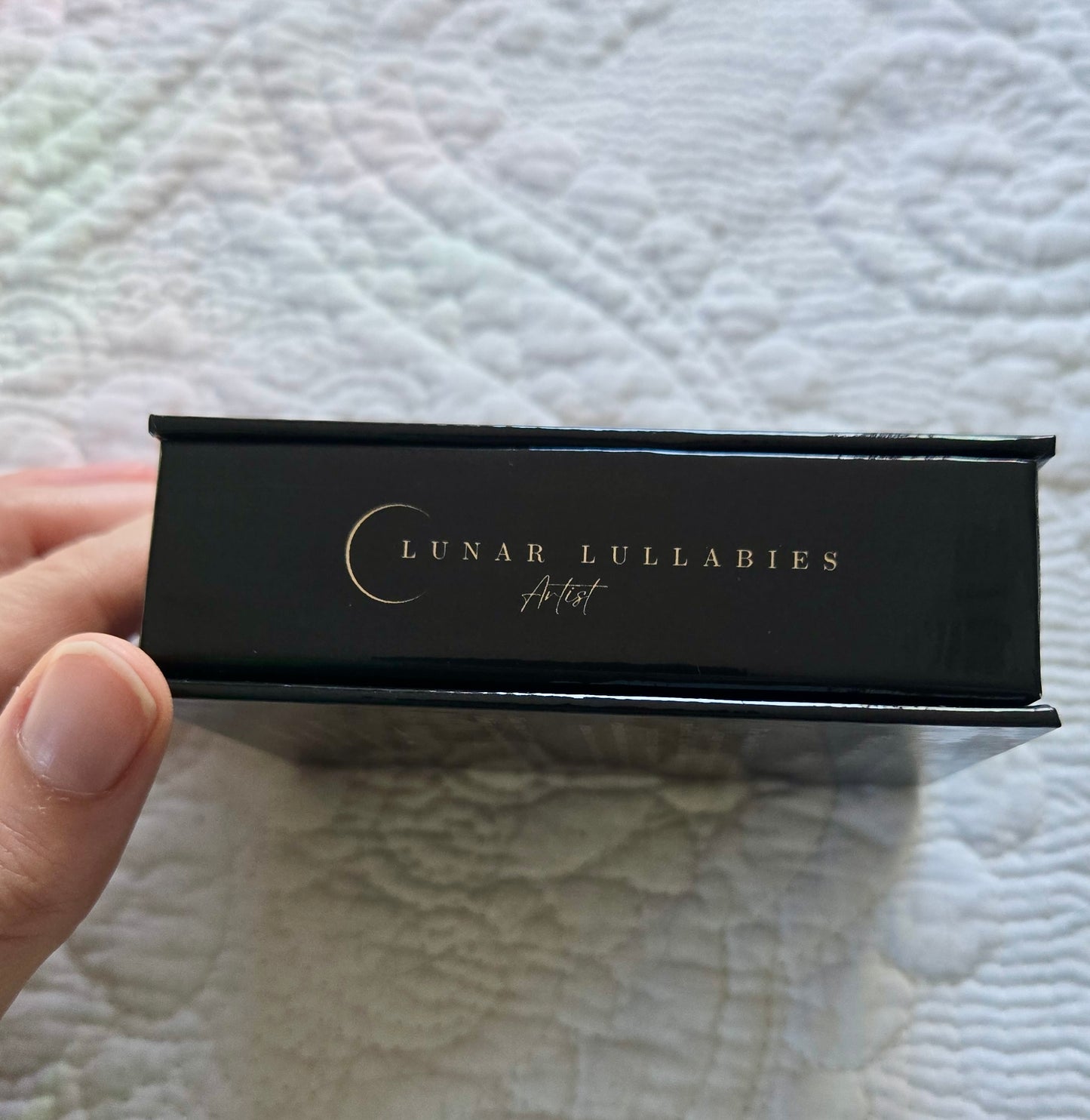 Black rectangular product box with 'Lunar Lullabies' branding held by a hand on a textured white background.