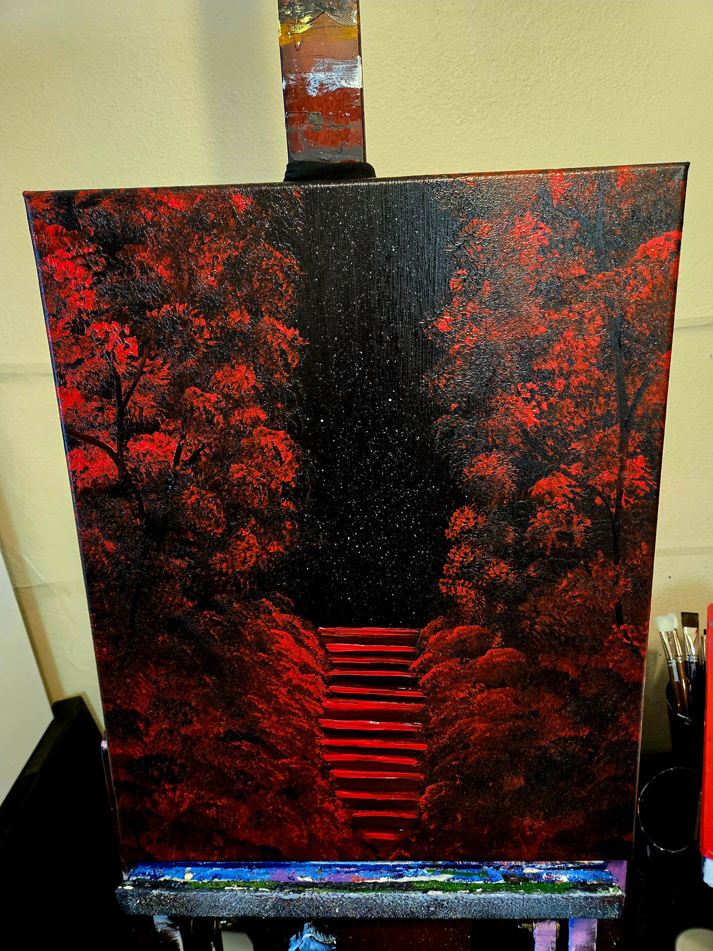 Painting on an easel of a red forest and red stars rising up through it