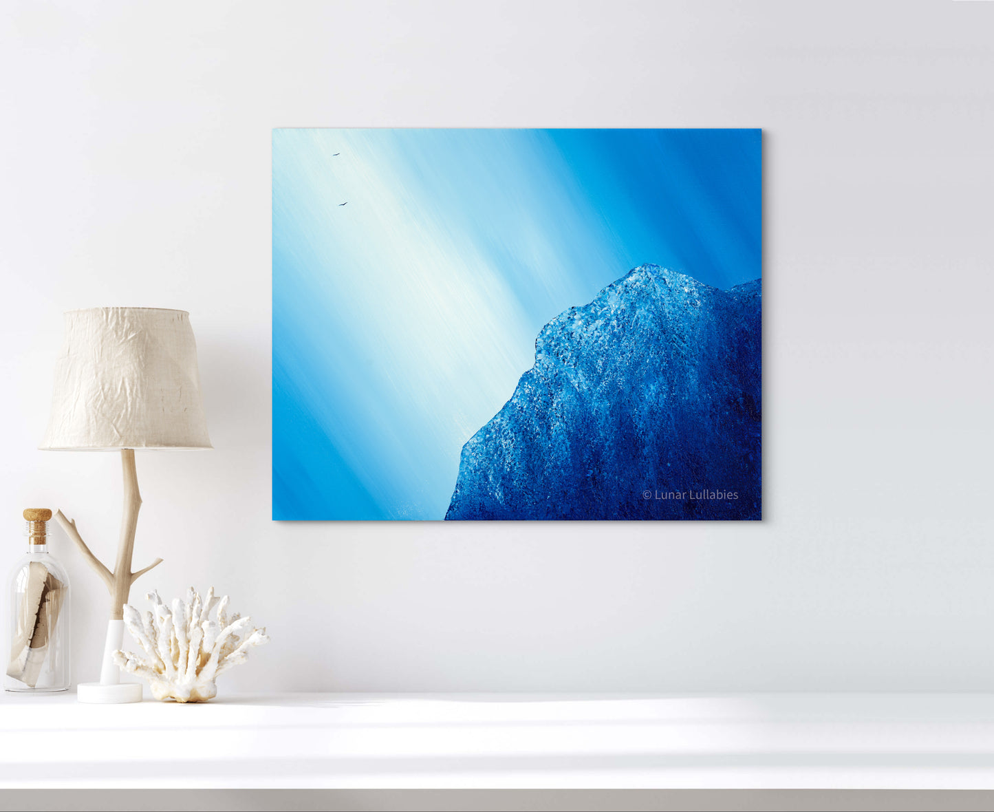 Mockup: Canvas print of a blue mountain and bird with sunlight on a white wall.