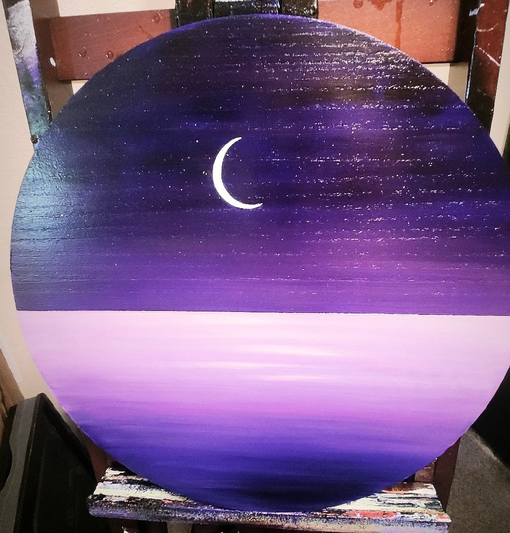 A wood panel painting on an easel with a purple ocean and sky and a crescent moon
