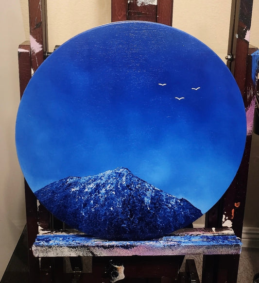 Round blue painting of a mountain and sky with birds on an easel 