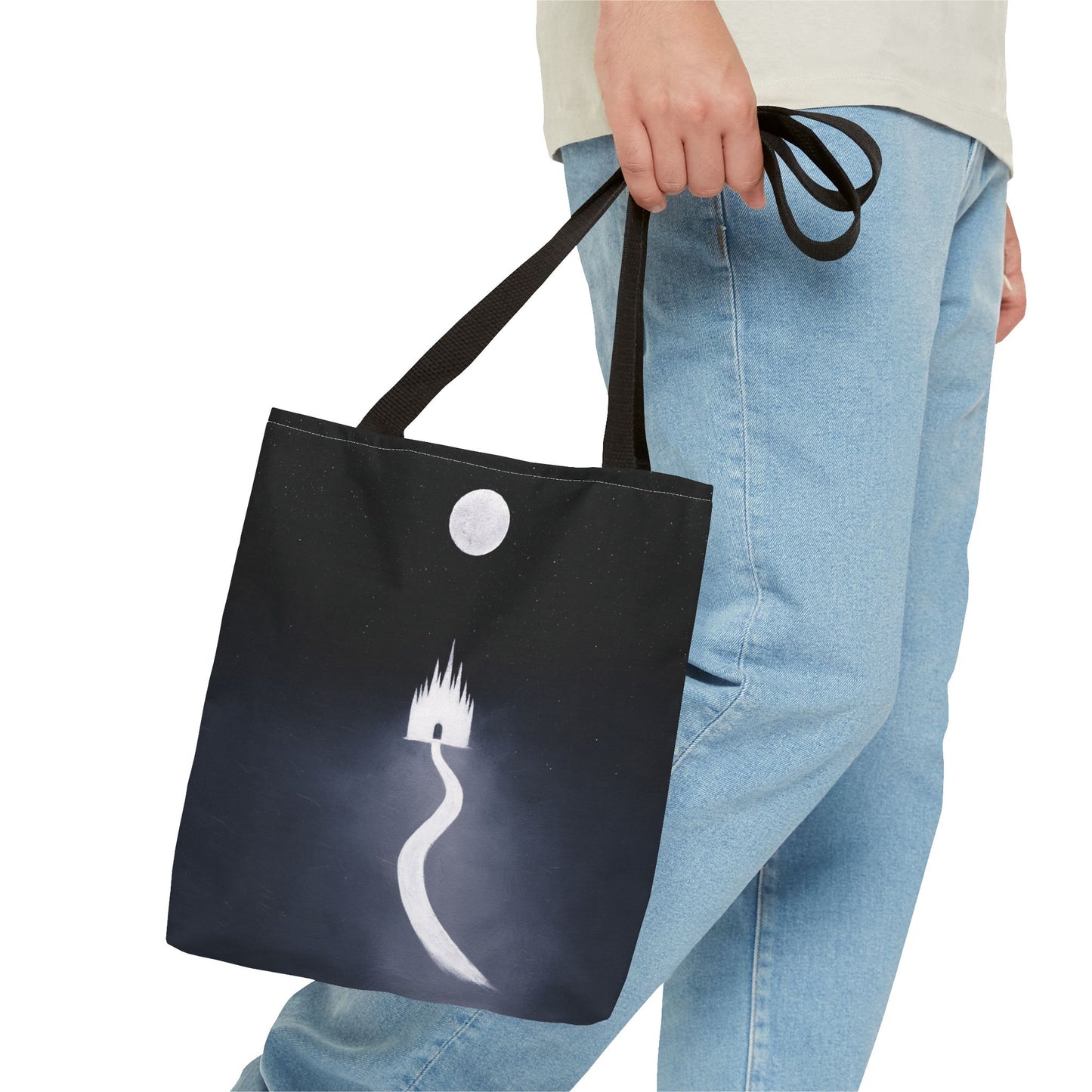 Person holding a black tote bag with a white design of a castle and moon on a white background