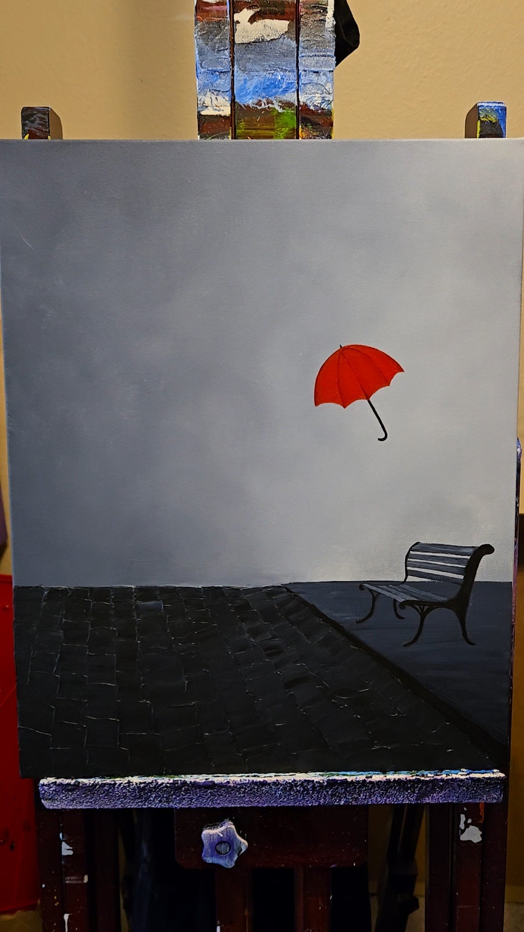 Painting of a red umbrella on a gray background with a bench below.