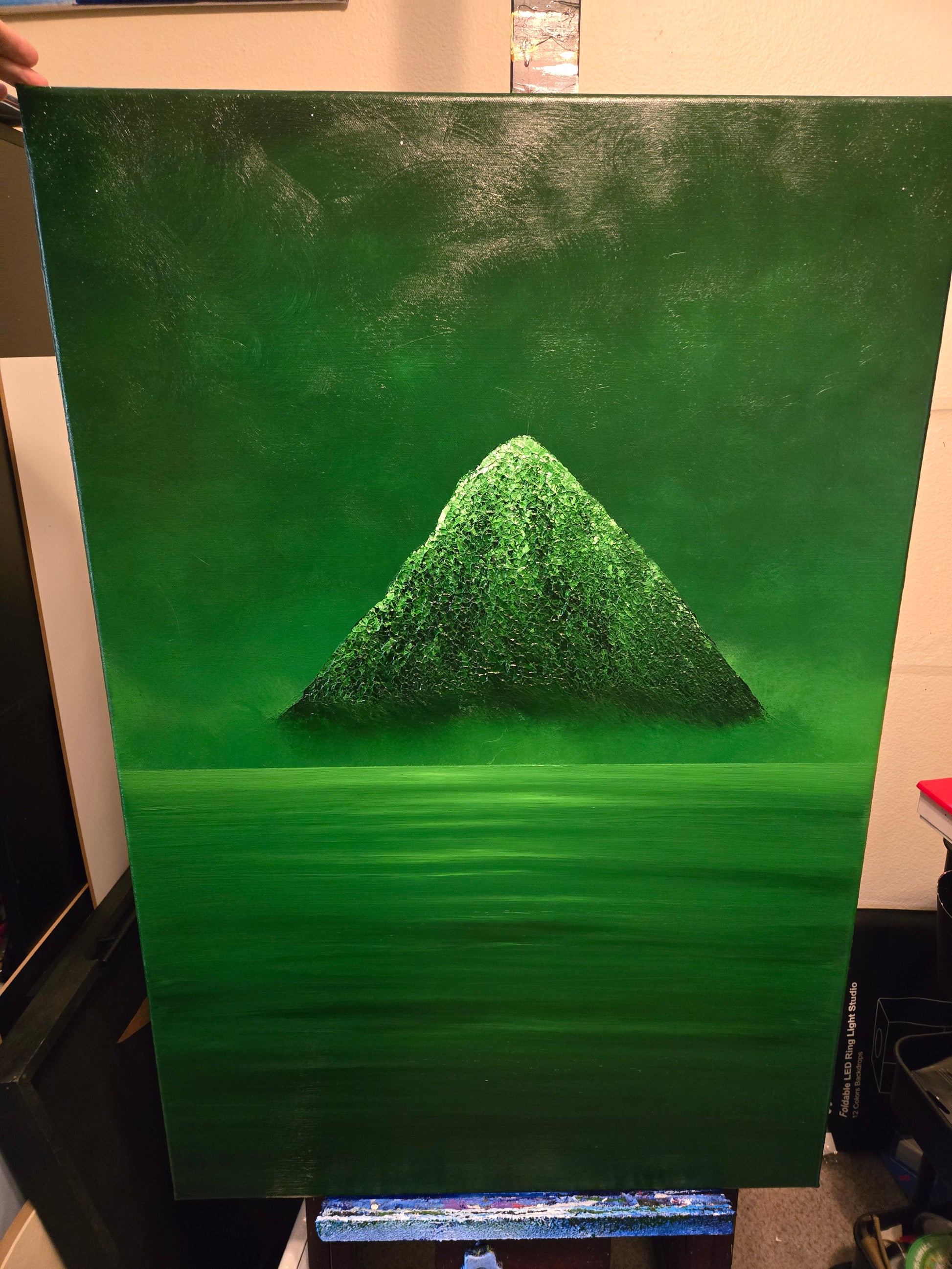 A green painting on an easel of a green mountain above a misty green ocean
