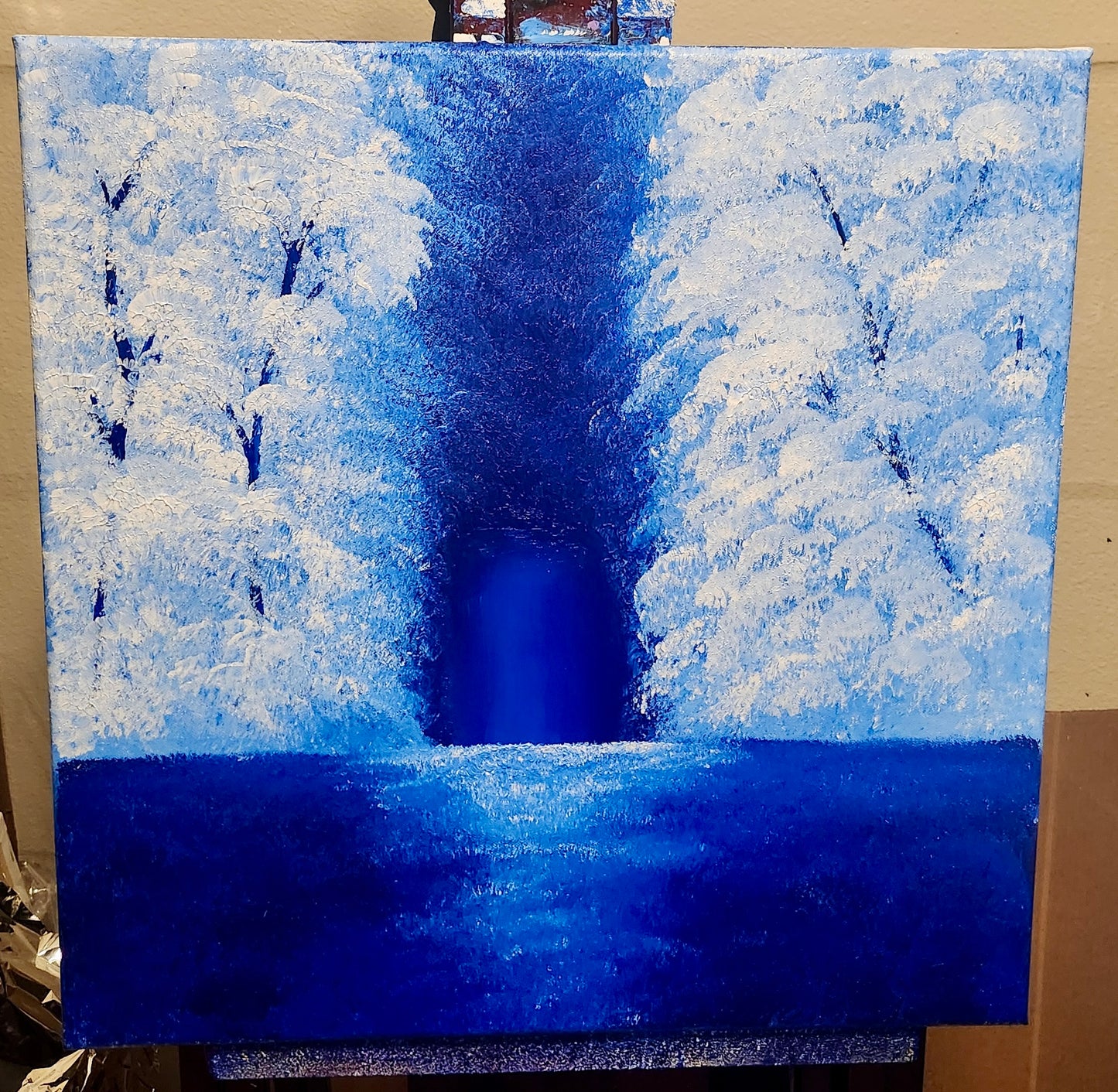Winter landscape painting with snow-covered trees and a dark blue sky on an easel.