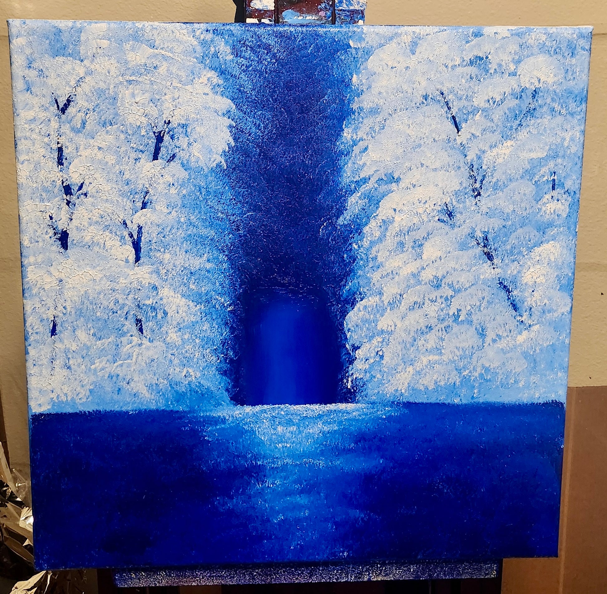 Winter landscape painting with snow-covered trees and a dark blue sky on an easel.